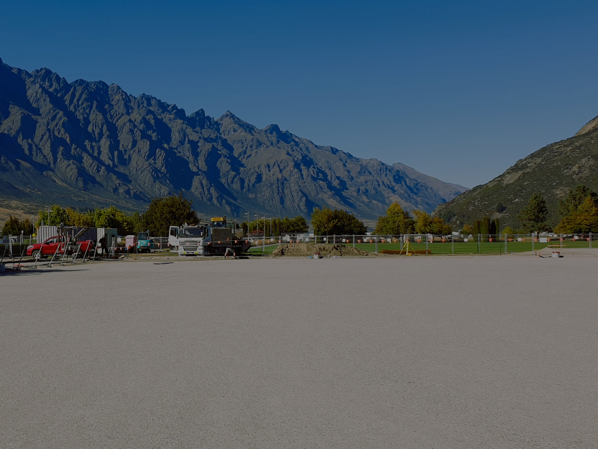 Ground photo of EDR Contracting completing Queenstown sports field development, showing smooth leveled base prepared for Polytan sports field material and turf with the Remarkables mountain range towering behind in summer light.